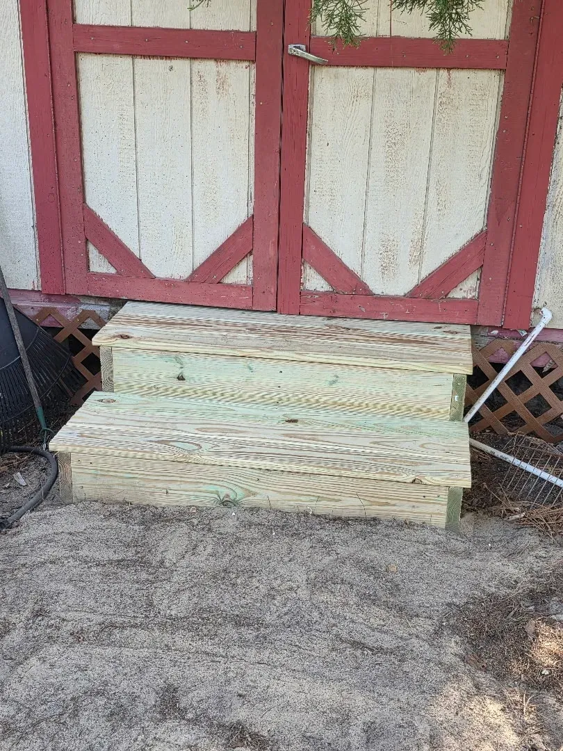 Wooden steps leading to a red-framed double door: exterior carpentry work in progress