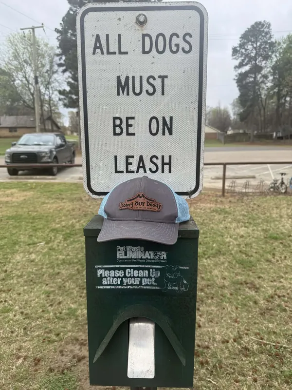 All Dogs Must Be On Leash sign mounted on a post next to a Pet Waste Eliminator disposal unit in a grassy area
