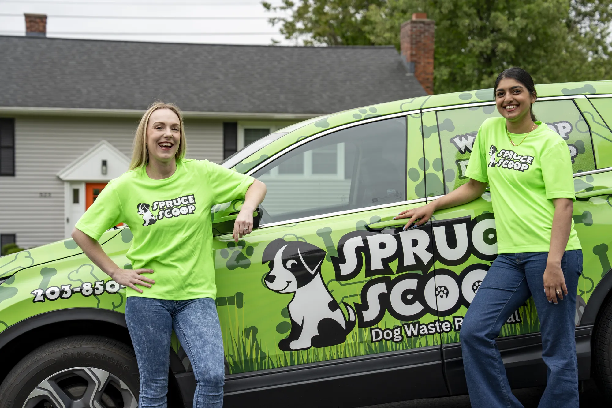 Two Spruce Scoop team members leaning on a wrapped Spruce Scoop car parked outside a house