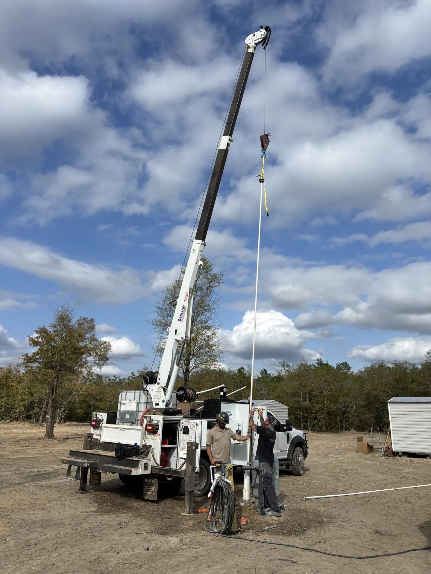 Crew operating a truck-mounted crane over a well on a job site