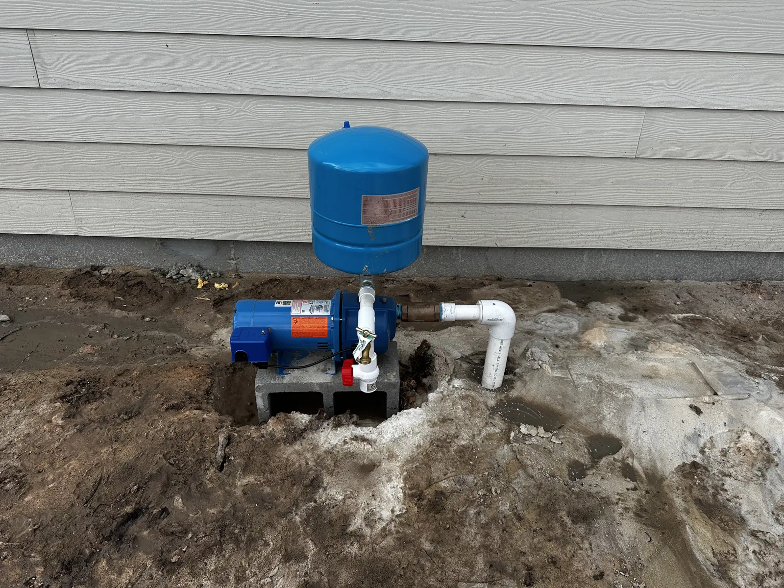 Finished blue well pump and pressure tank installed outside a home
