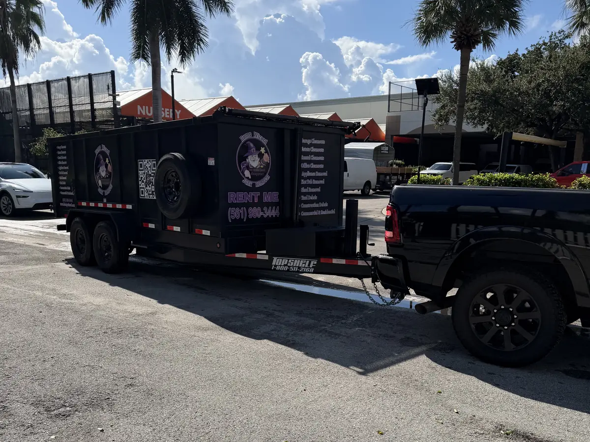 Dump Wizard RENT ME trailer hitched to a black pickup truck at a Fort Lauderdale job