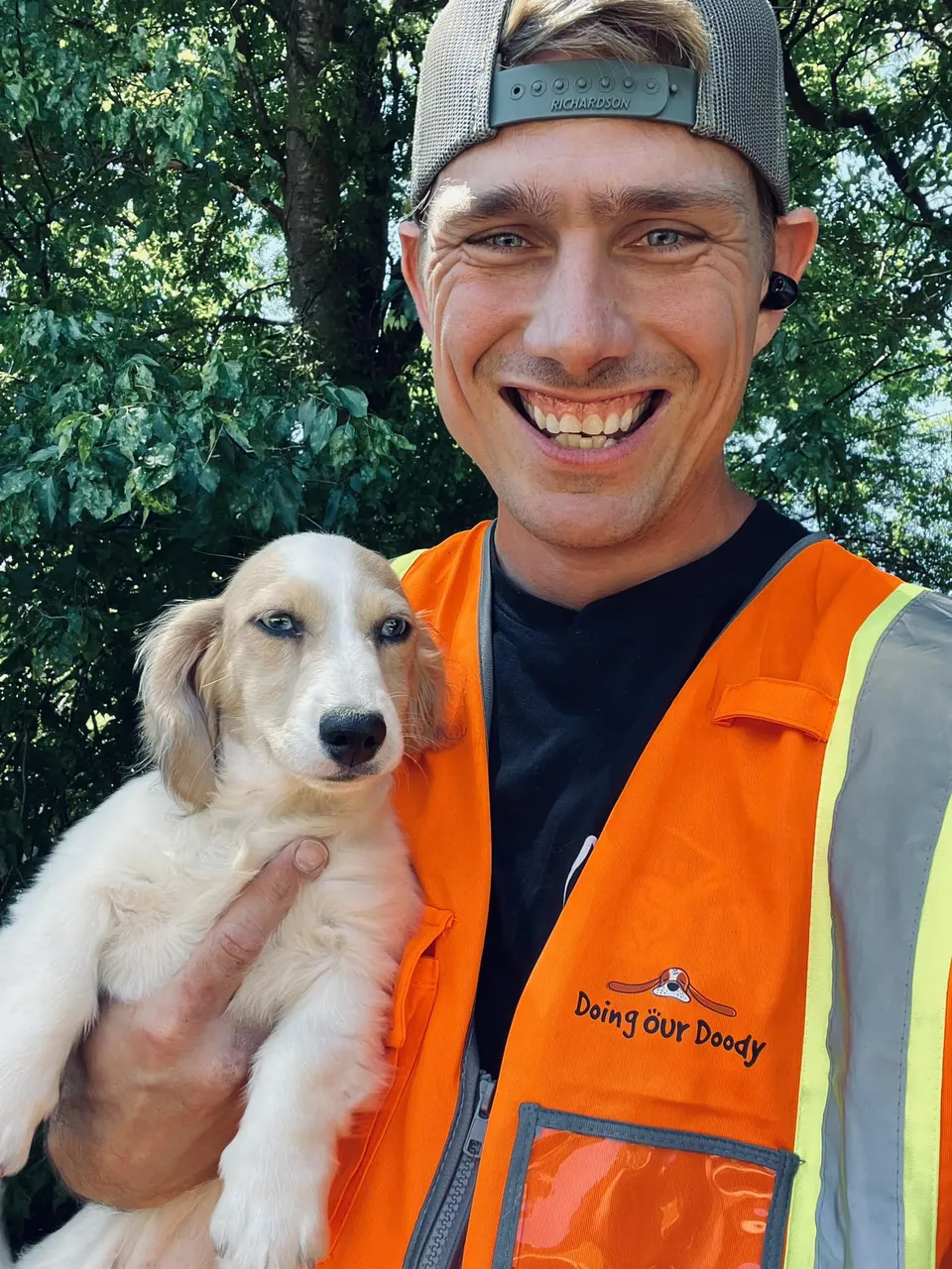Willum smiling in an orange safety vest, holding a small puppy on a Texas property
