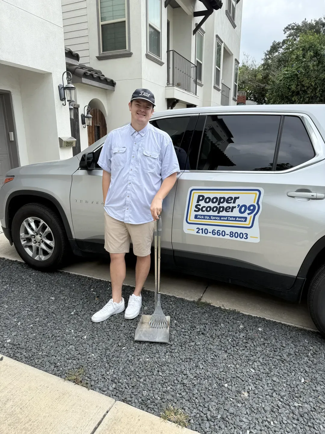 B.P. Foley standing on a driveway beside the silver Pooper Scooper '09 SUV, holding a rake and a waste pan