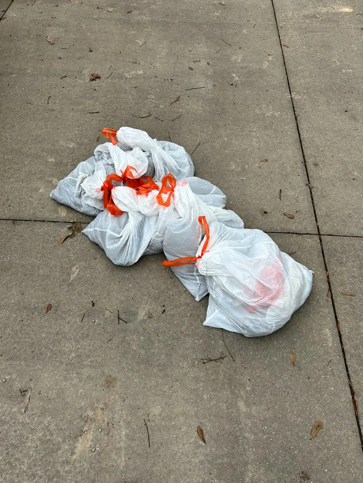 A pile of tied white waste bags on concrete pavement