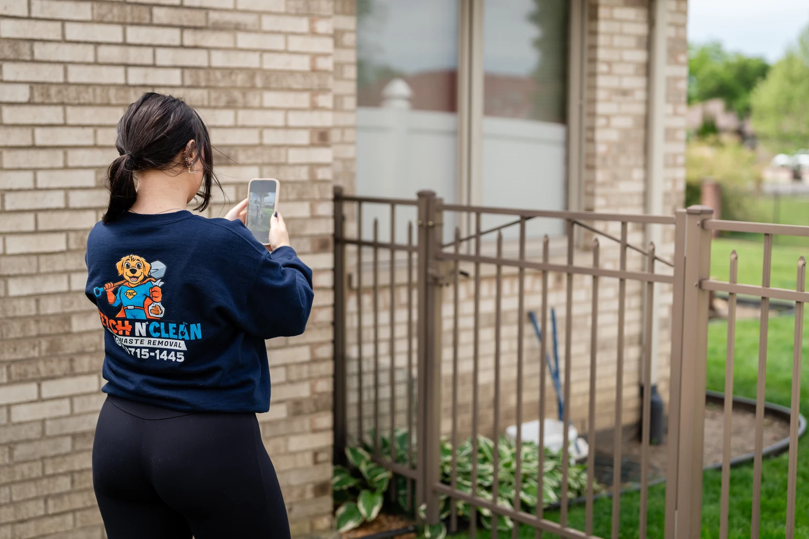 Fetch N Clean team member using a phone near a fenced yard.