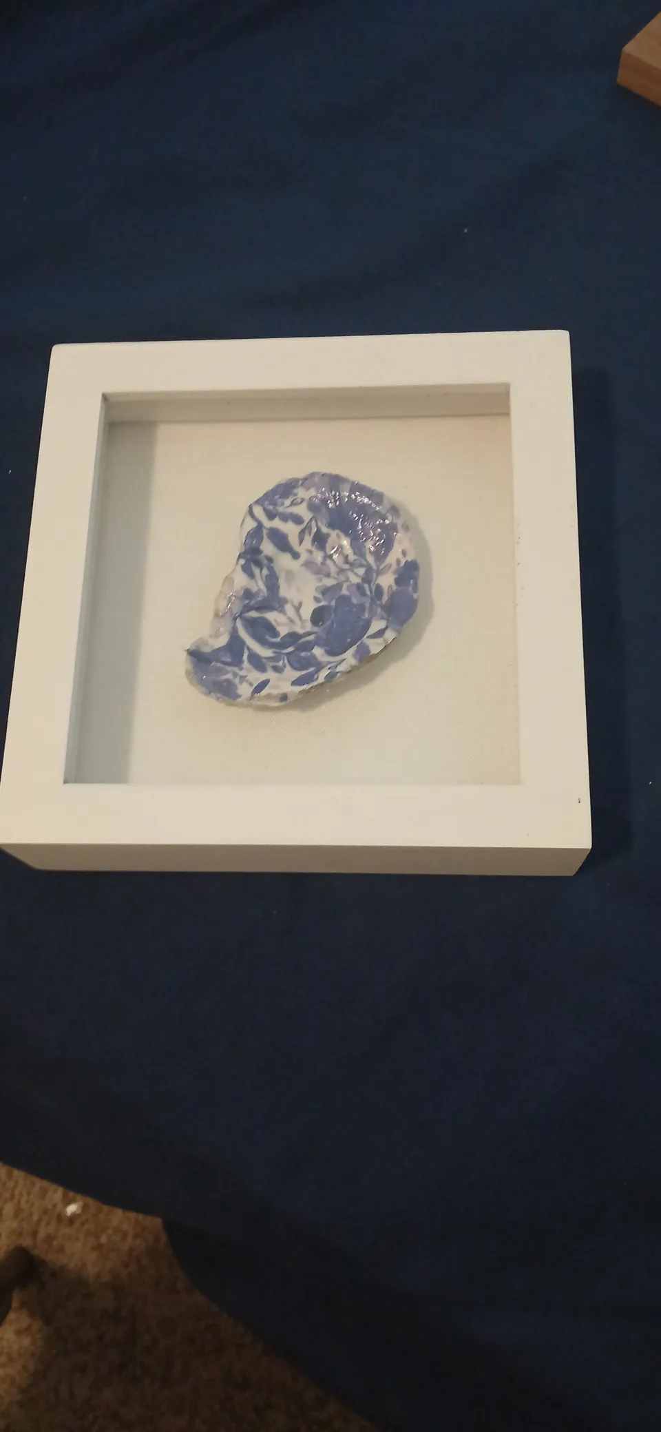 White shadow box containing an oyster shell with a blue and white floral pattern