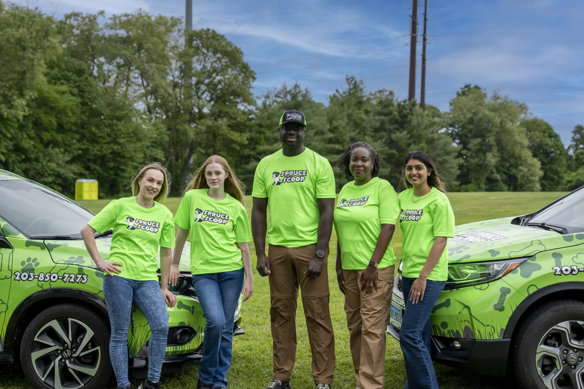 Five Spruce Scoop team members in green shirts with two wrapped Spruce Scoop cars