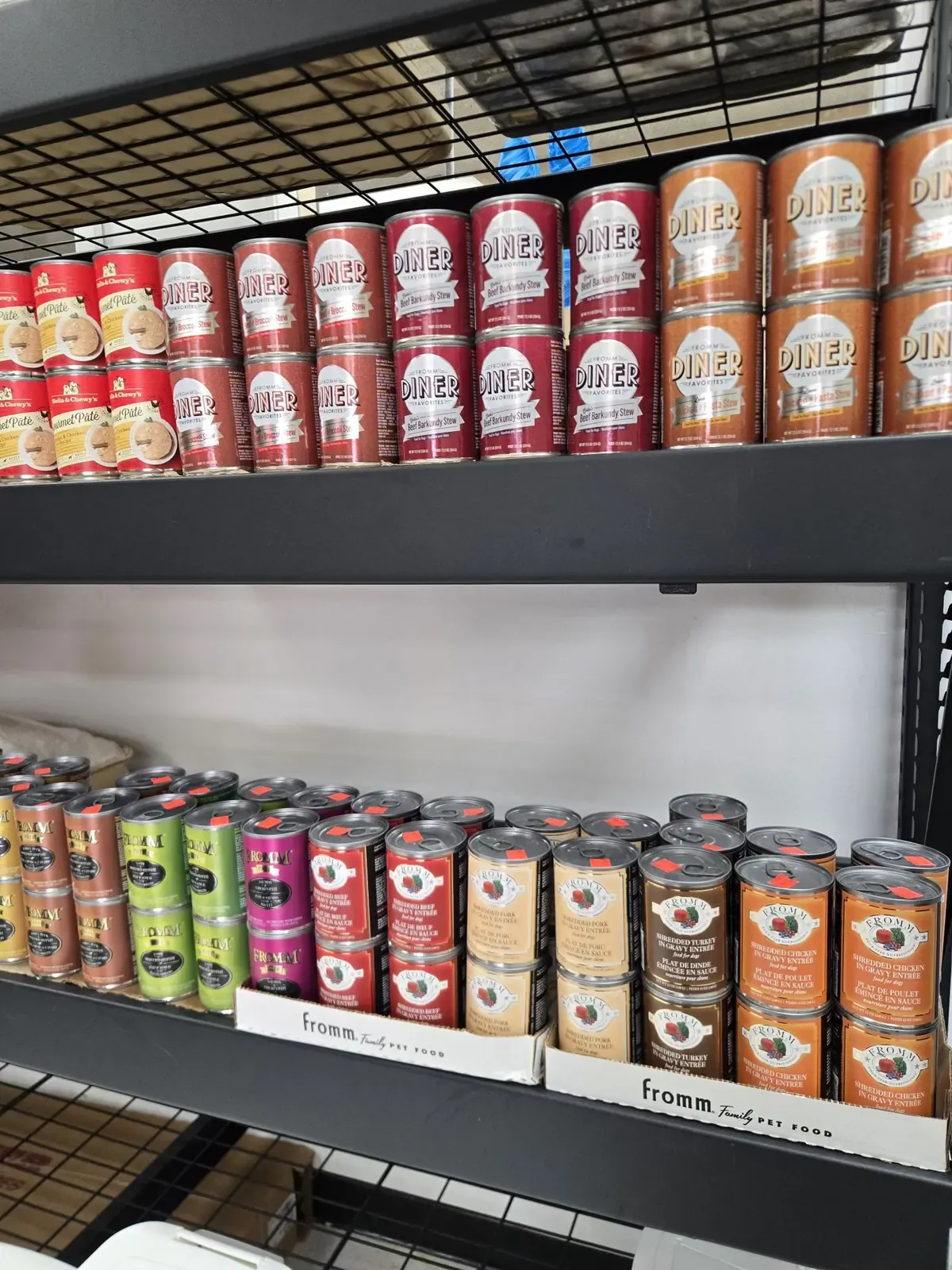 Canned dog food from Stella & Chewy's and Fromm, including Fromm Diner Favorites stews and Four-Star shredded entrées, on the shelves at Dog O Mat