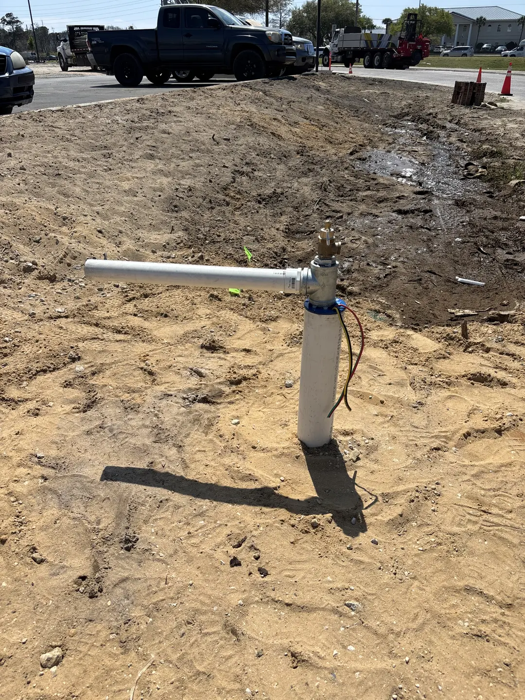 Newly installed wellhead with white vertical casing pipe on a sandy site