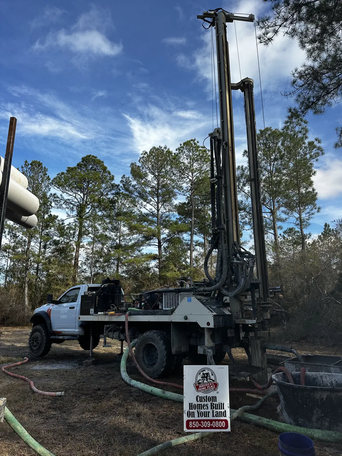 Water well drilling rig and support truck staged in a stand of pines