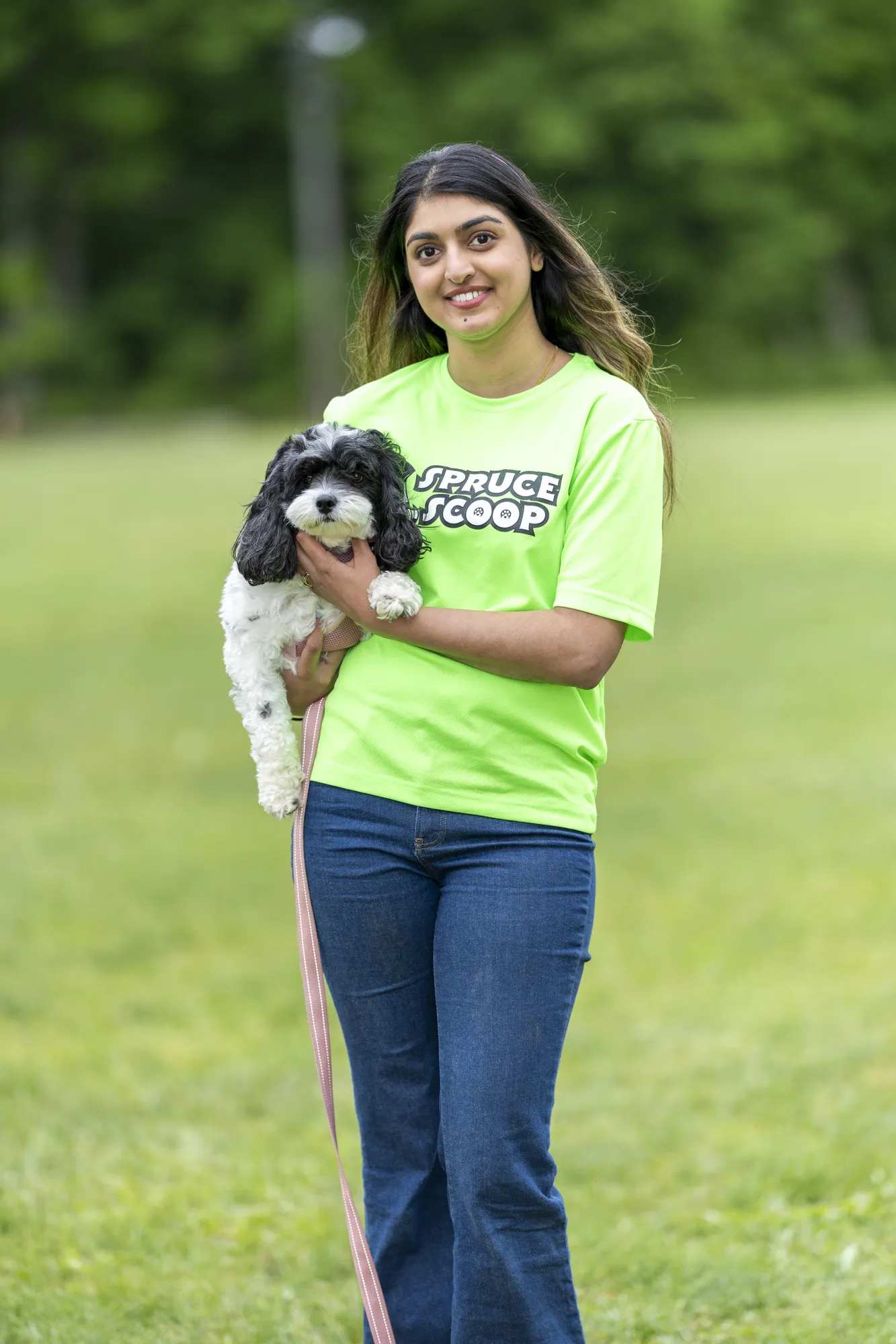 A Spruce Scoop team member holding a small black-and-white dog on a grassy field