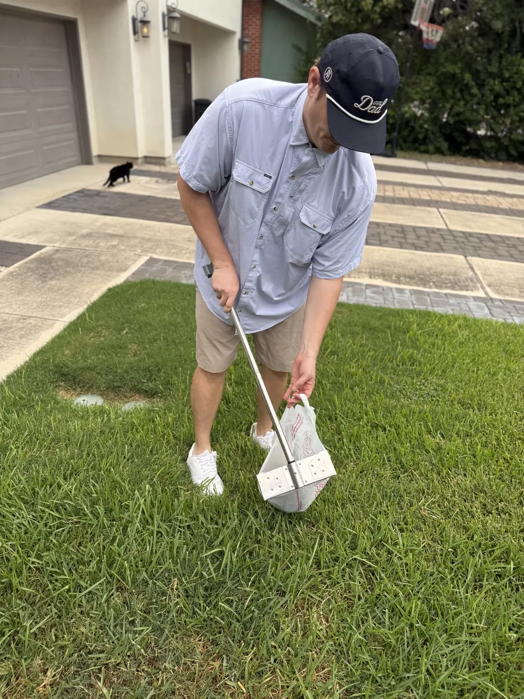 B.P. Foley bending over a lawn with a waste pan and a bag, picking up pet waste