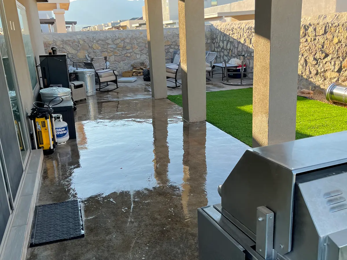 Covered back patio with wet concrete next to an artificial turf lawn