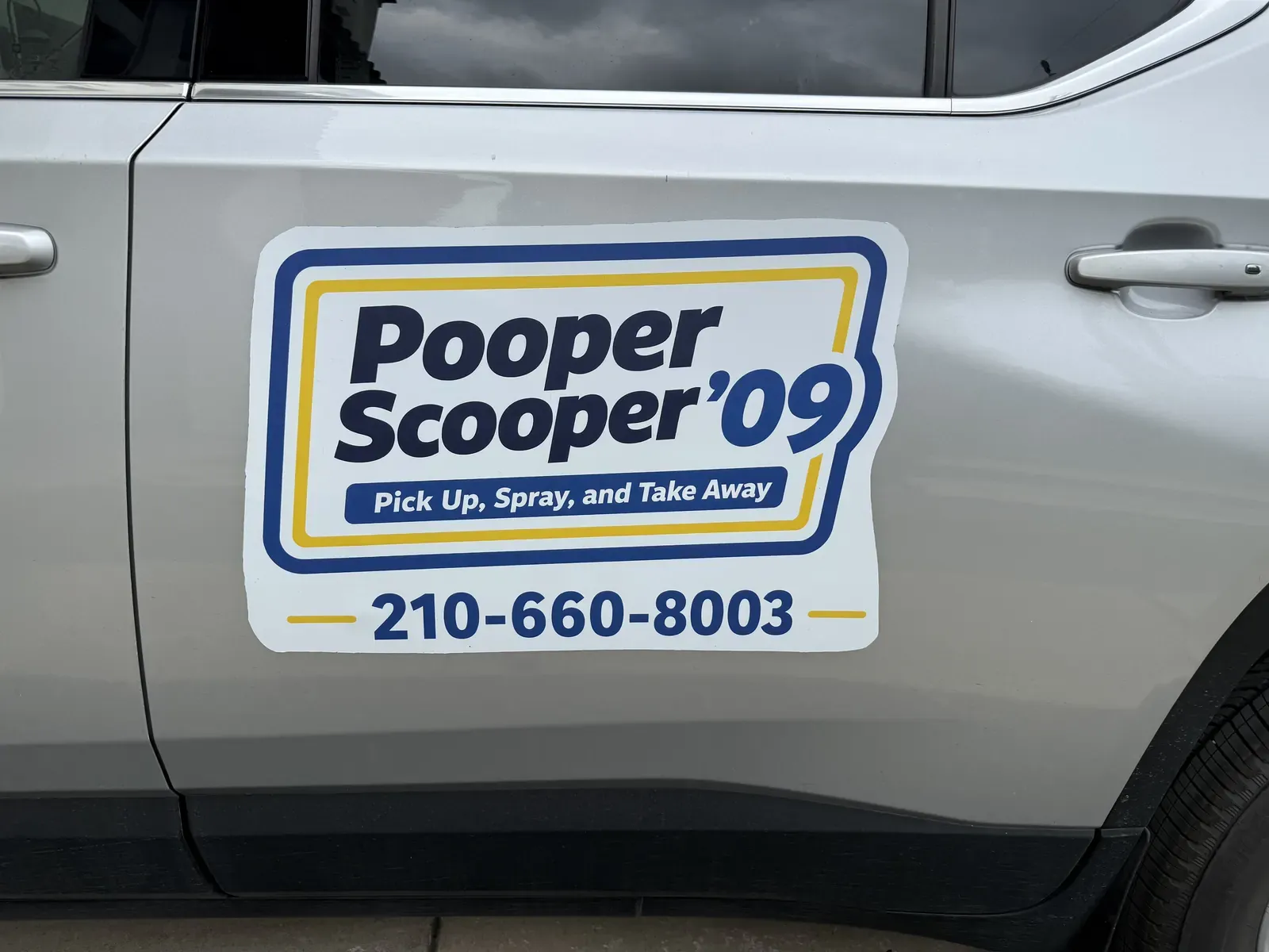 The Pooper Scooper '09 logo, slogan, and phone number 210-660-8003 on the door of the silver SUV
