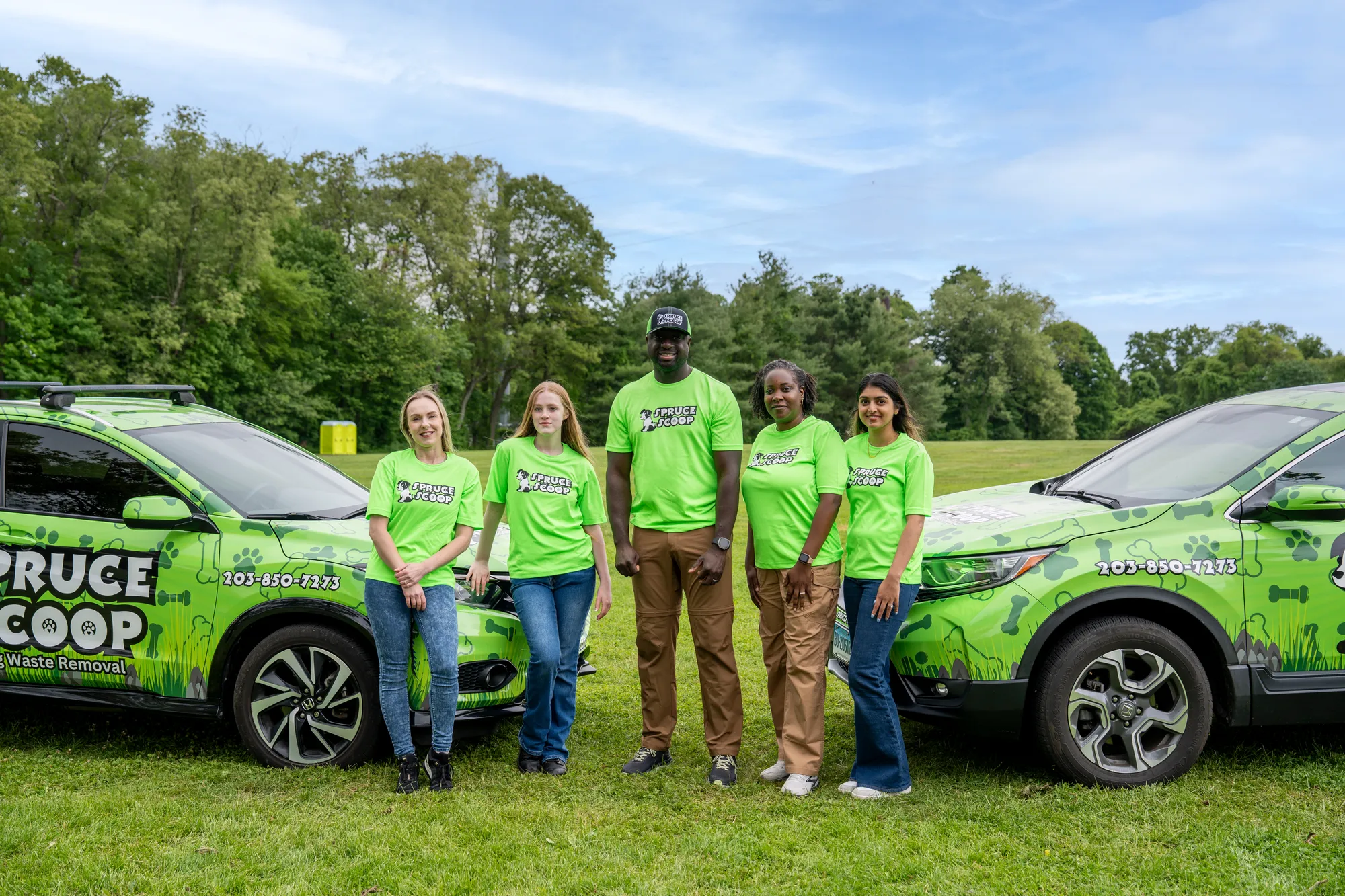 Five Spruce Scoop team members standing on a lawn between two wrapped Spruce Scoop cars