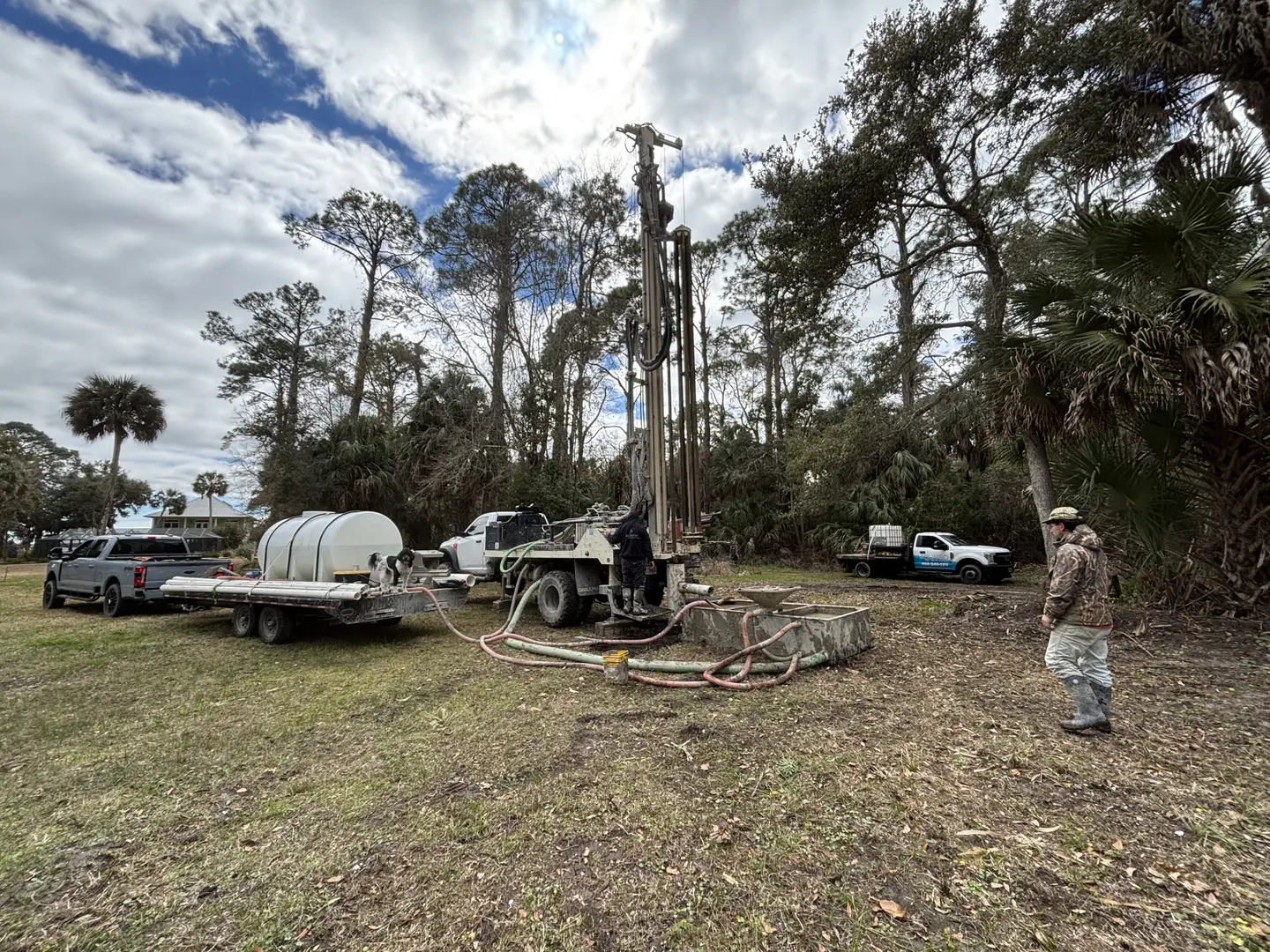 Drilling rig and support trucks on an active wooded job site