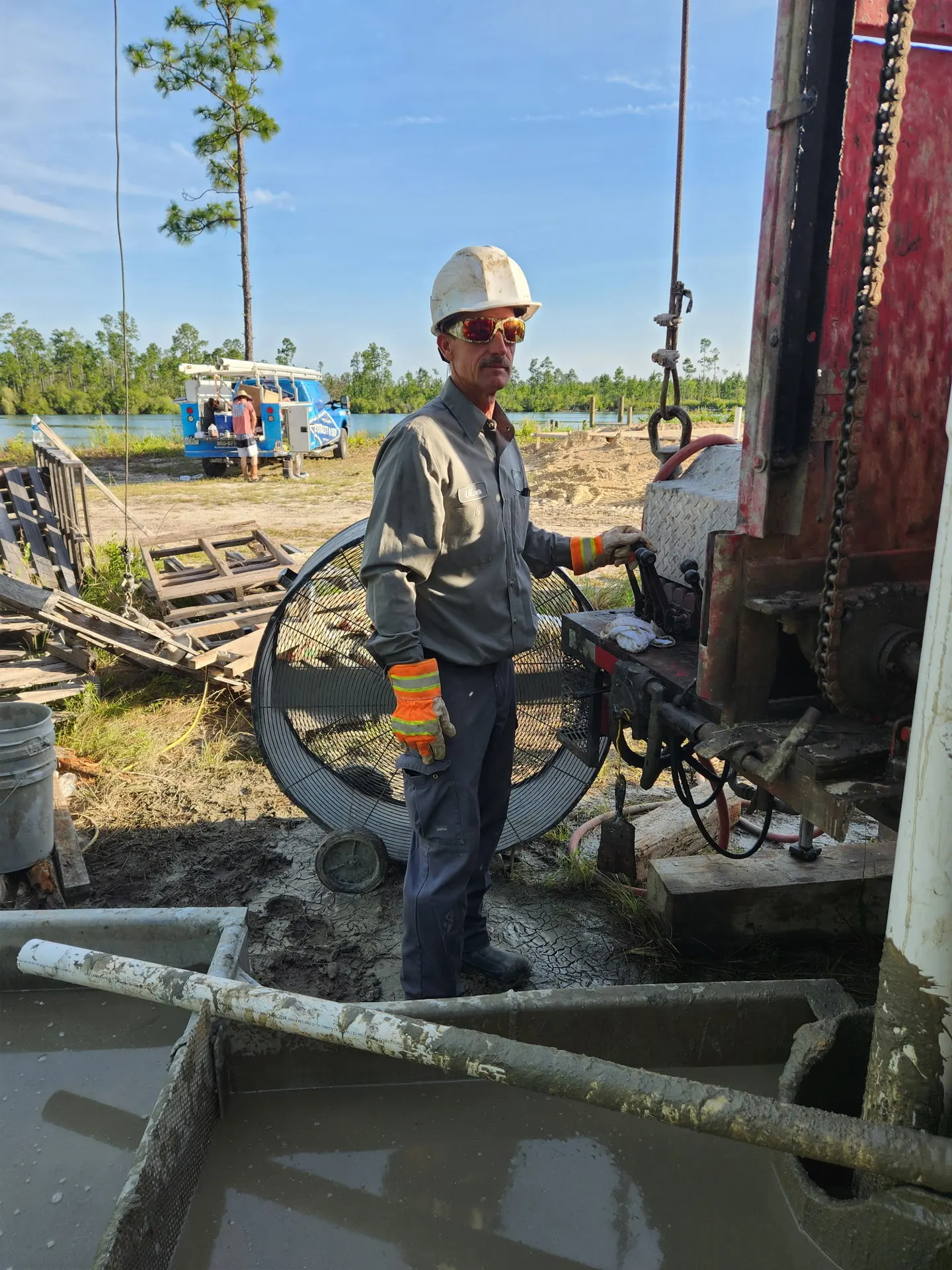 Worker in safety helmet standing beside drilling equipment near the water