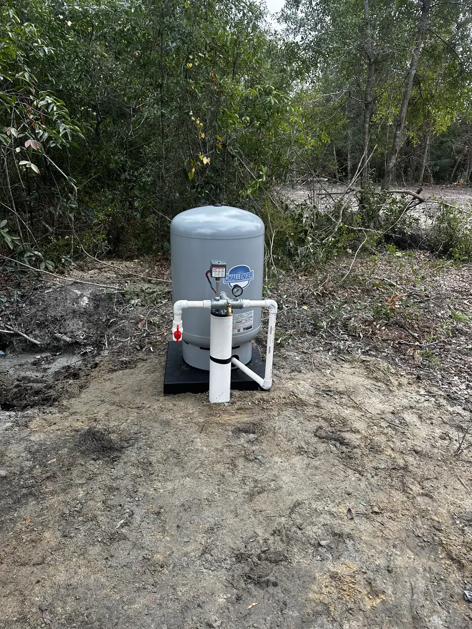 Gray pressure tank plumbed in white PVC surrounded by greenery