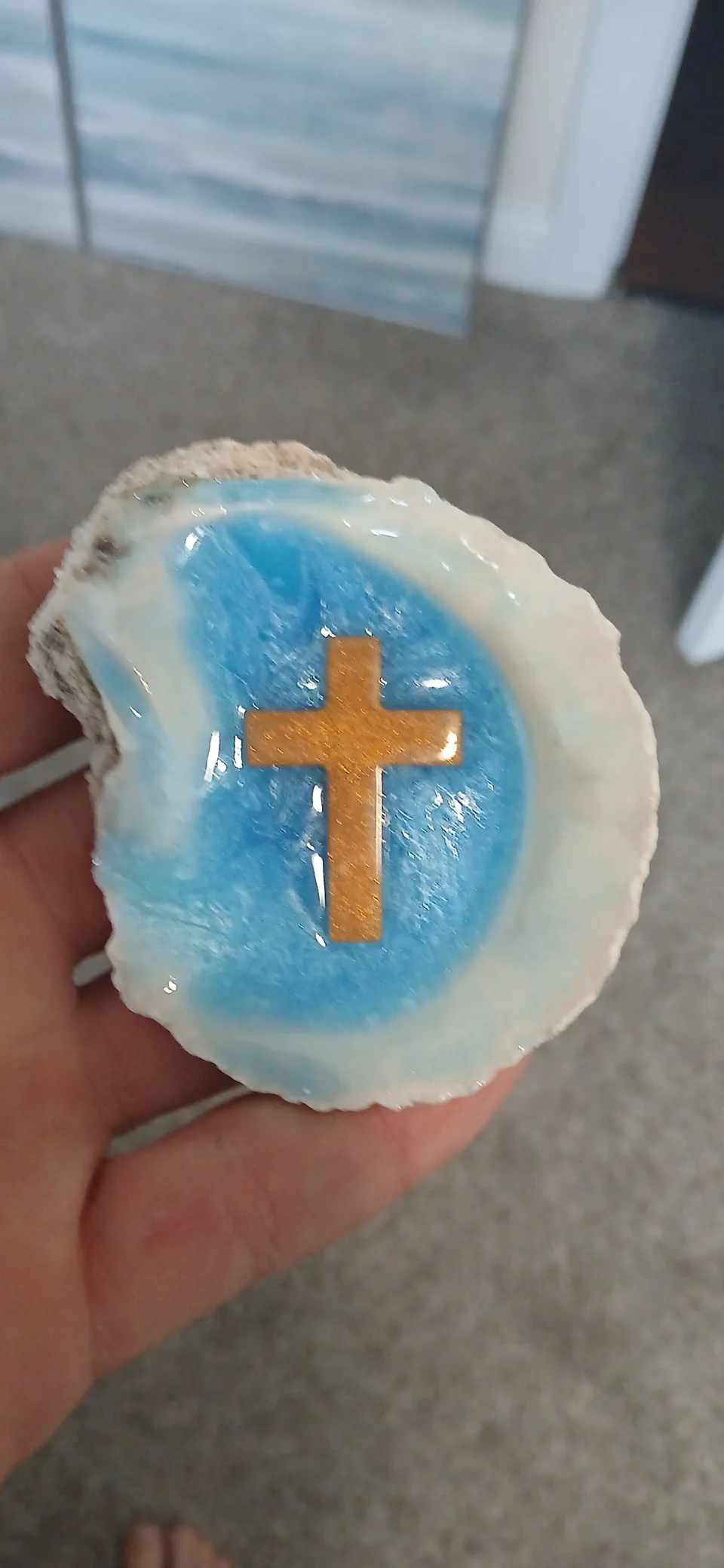 Hand holding a white oyster shell with a blue center and a gold-colored cross