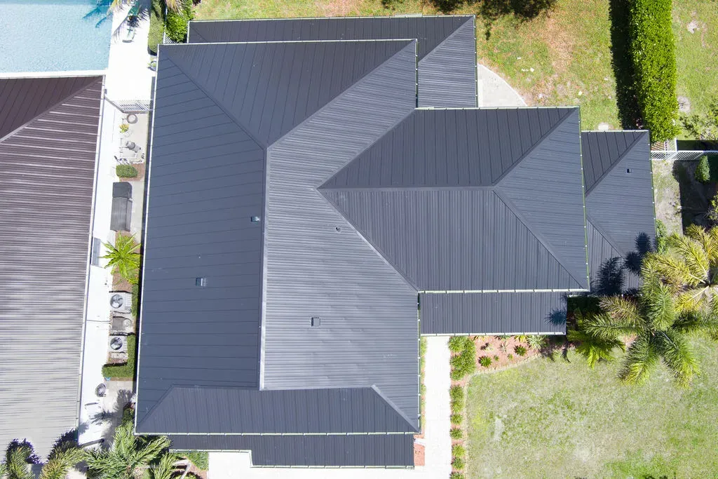 Aerial view of two modern homes featuring sleek black metal roofs with surrounding greenery and pool