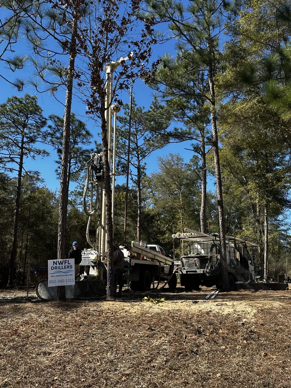 NWFL Drillers rig raised among tall pines, crew preparing to drill