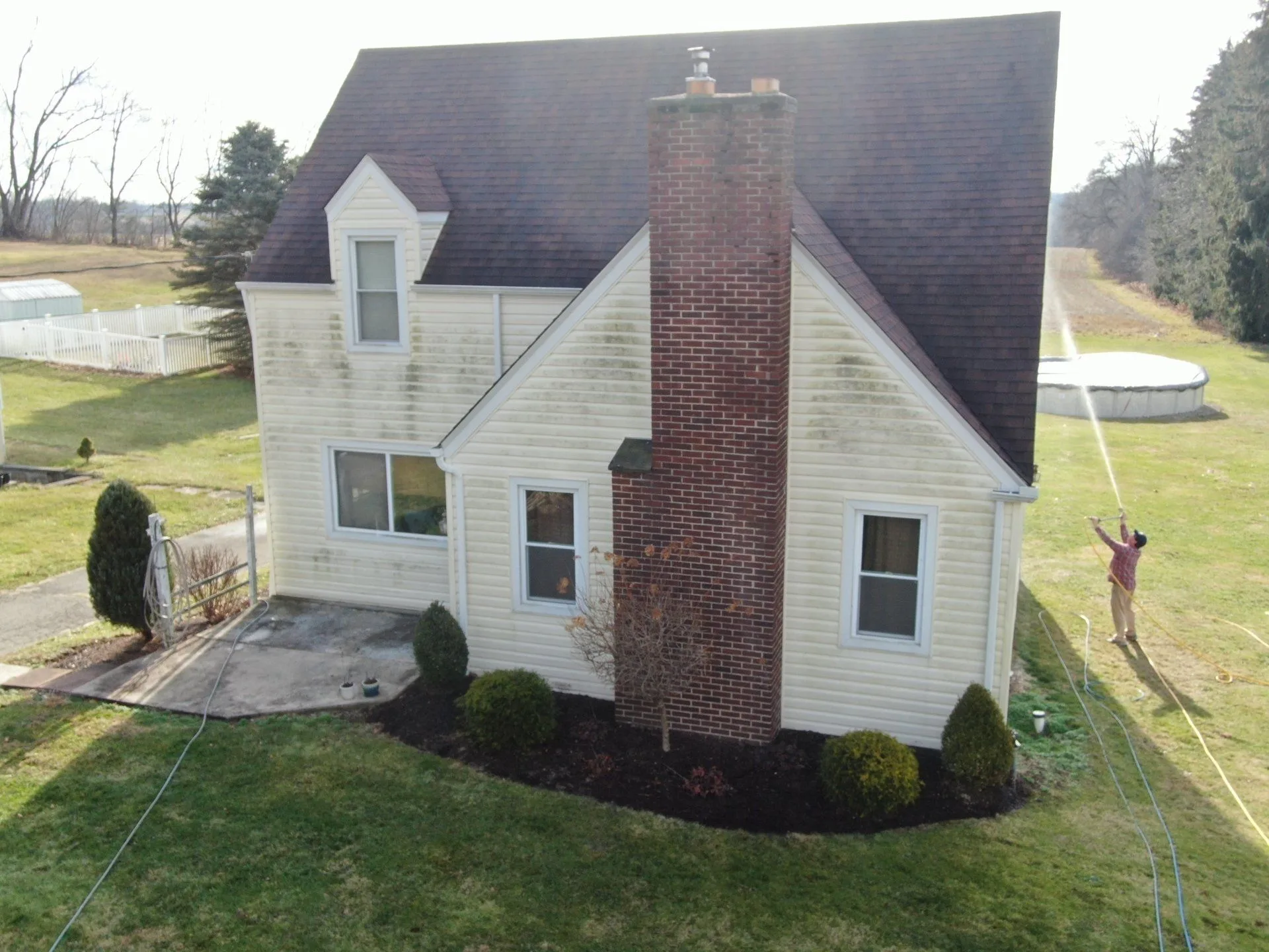 House exterior before washing, with visible buildup and a worker cleaning the siding