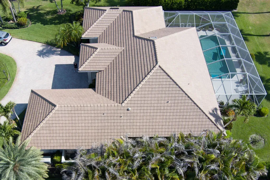 Aerial drone view of a single-story Florida home with clay tile roof, screened pool and tropical landscaping