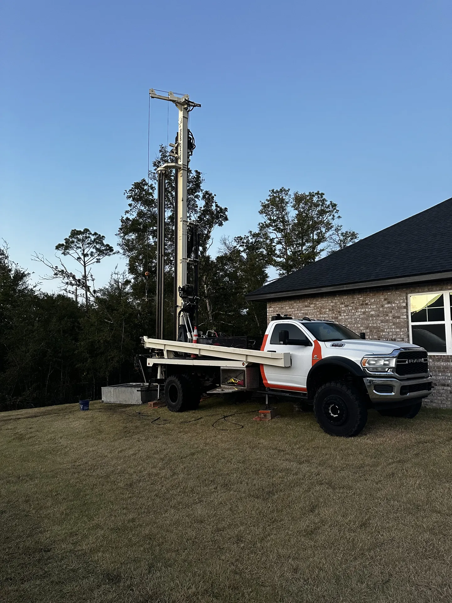 Specialized drilling truck with a tall rig parked next to a house