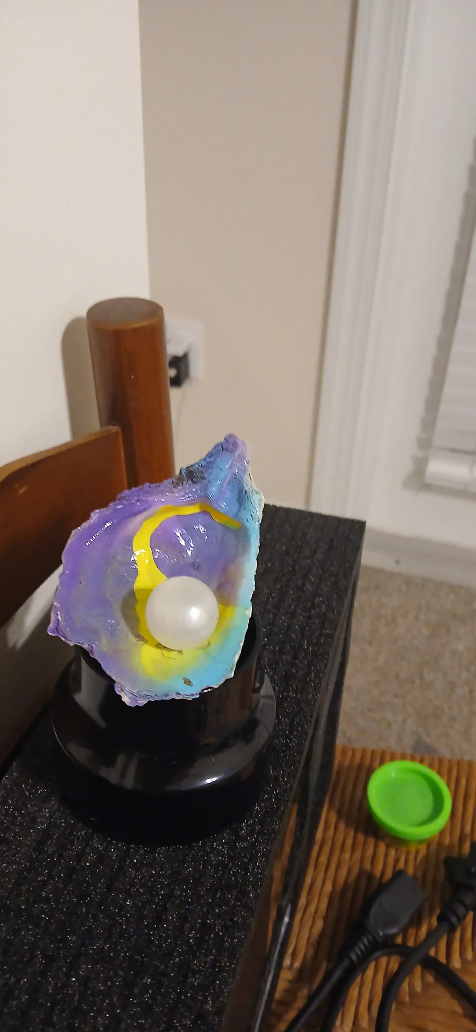 Purple, blue and yellow shell with a round white bead, displayed on a dark base
