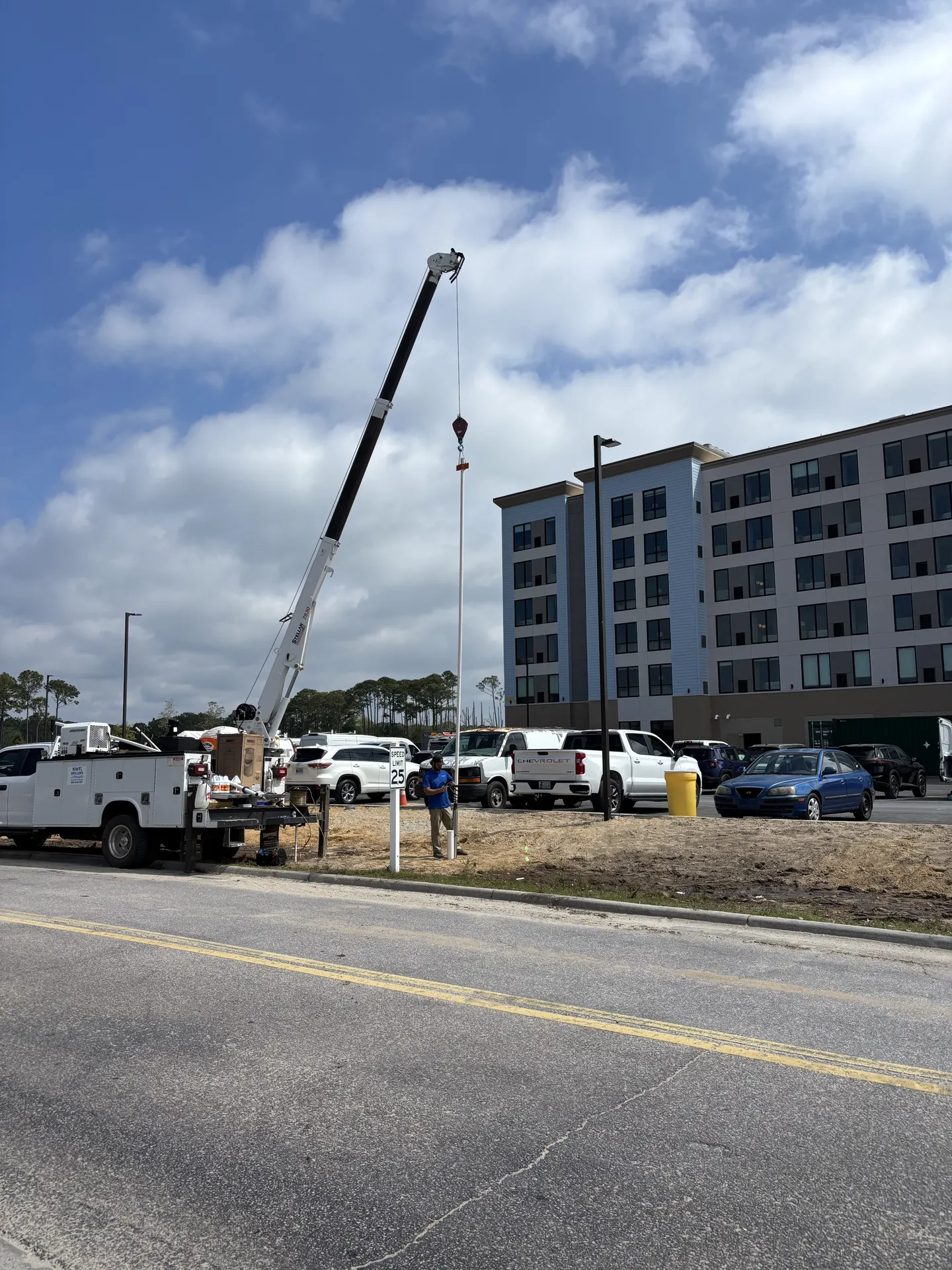 Crane lifting a vertical pole at a construction site with a multi-story building in the background