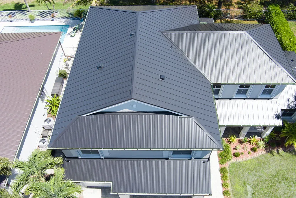 Aerial drone view of multiple modern Florida homes with sleek black and silver standing-seam metal roofs and a pool