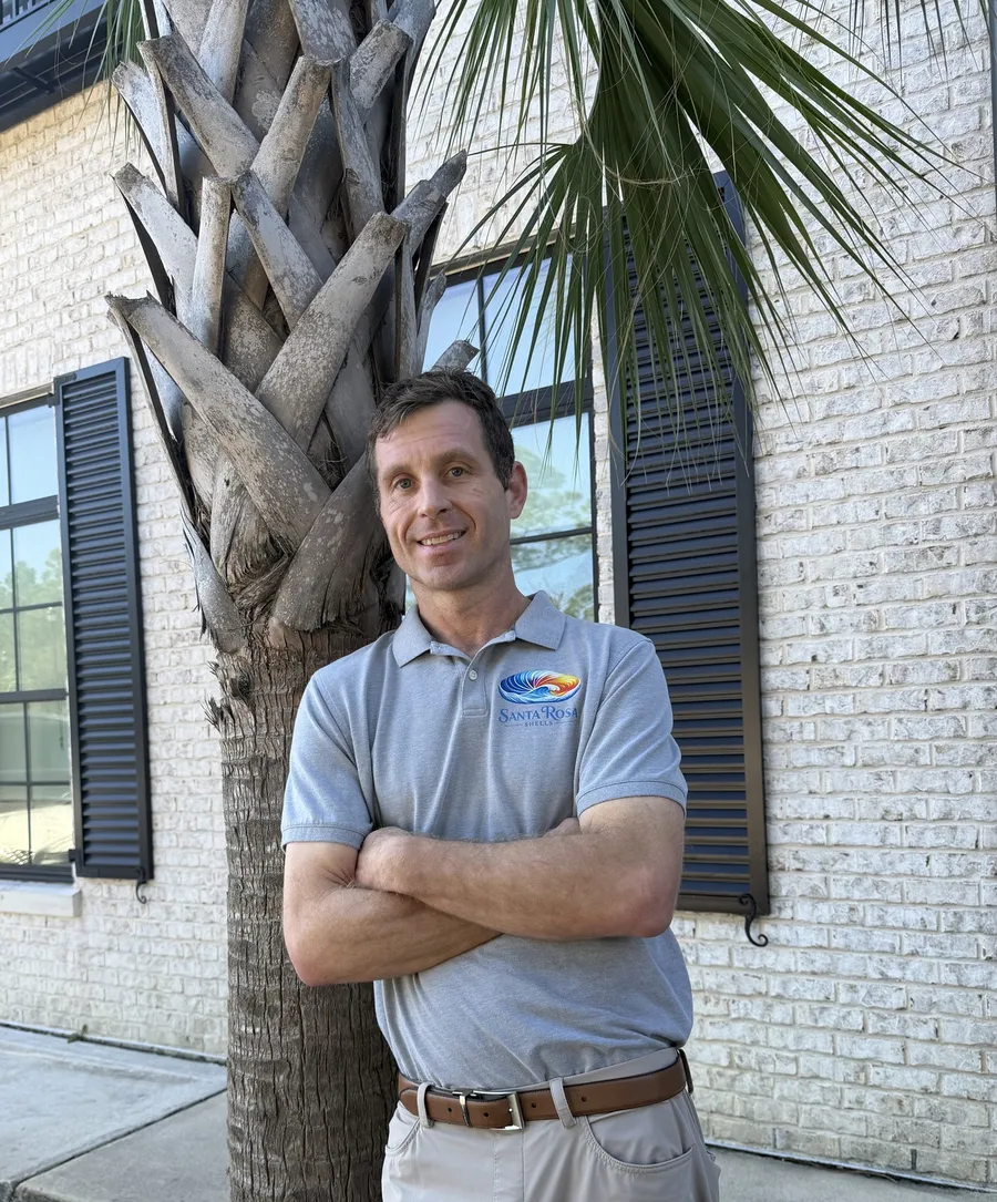 Zak wearing a Santa Rosa Shells polo beside a palm tree