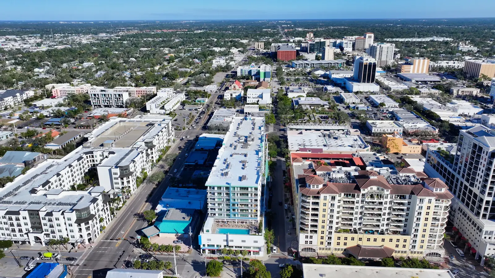 Aerial perspective of a bustling urban area featuring a mix of modern residential buildings and commercial spaces. The scene includes greenery in the background, highlighting the blend of city life and nature.