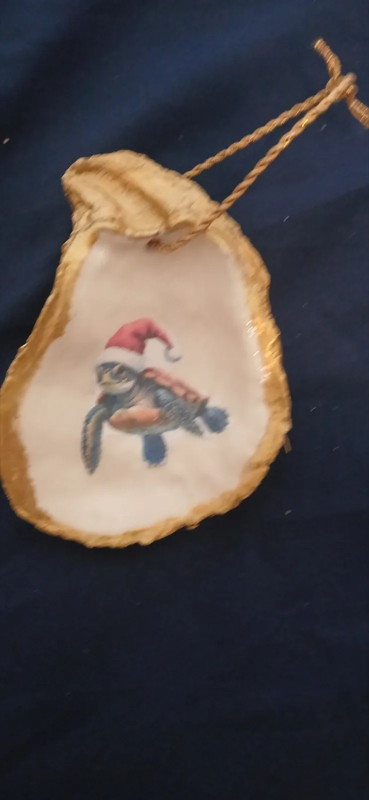 Gold-edged oyster shell ornament showing a sea turtle in a Santa hat, hanging from a twisted cord