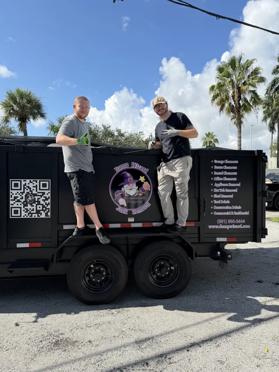 Two Dump Wizard crew members giving a thumbs up from the side of the wrapped trailer