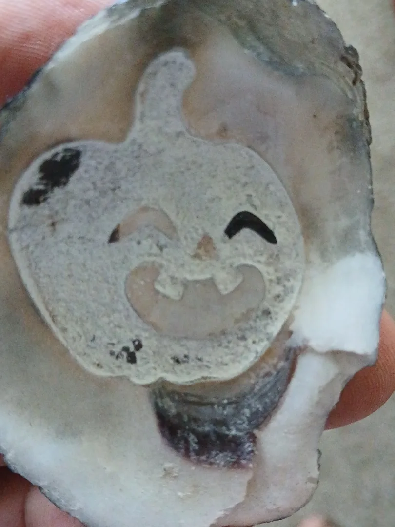 Hand holding an oyster shell engraved with a smiling jack-o-lantern