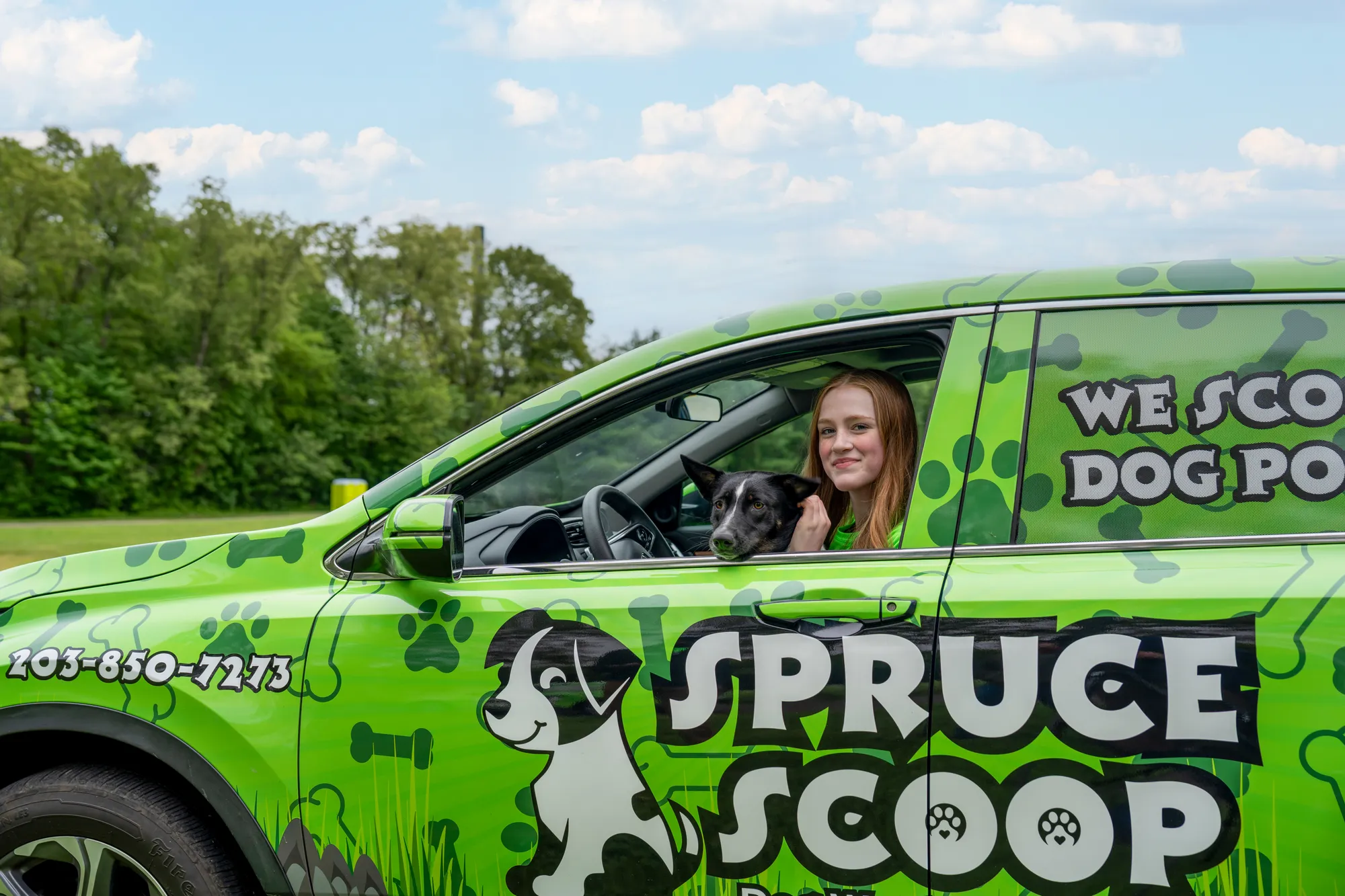 A Spruce Scoop team member and a black-and-white dog in the front seat of a wrapped Spruce Scoop car