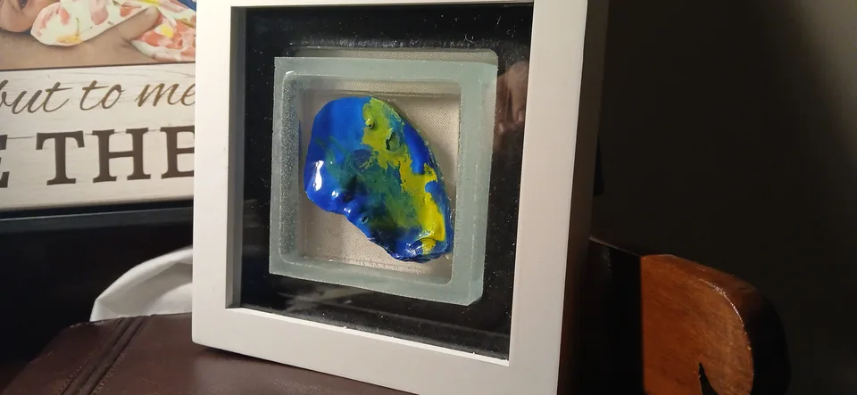 White shadow box holding a blue, green and yellow oyster shell inside a smaller pale frame